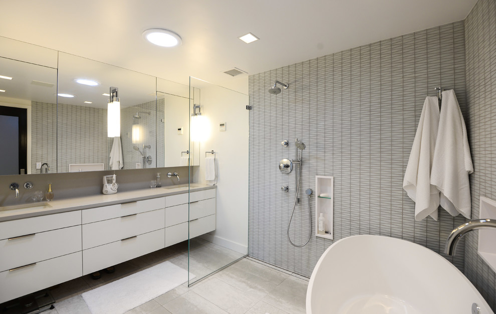 Bild på ett funkis grå grått en-suite badrum, med släta luckor, vita skåp, ett fristående badkar, en öppen dusch, grå kakel, vita väggar, ett undermonterad handfat, grått golv och med dusch som är öppen