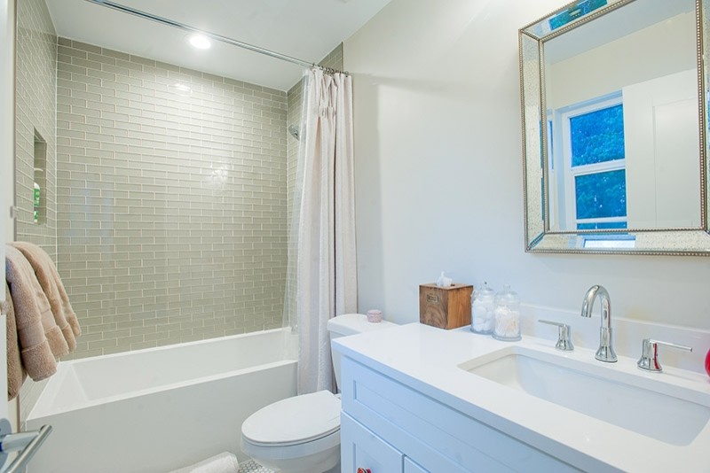 Foto på ett mellanstort minimalistiskt badrum med dusch, med skåp i shakerstil, vita skåp, ett badkar i en alkov, en dusch/badkar-kombination, en toalettstol med separat cisternkåpa, grå kakel, tunnelbanekakel, vita väggar, mosaikgolv, ett undermonterad handfat, bänkskiva i akrylsten, vitt golv och dusch med duschdraperi