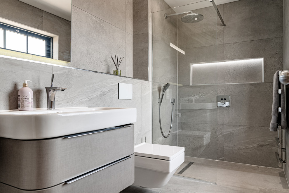 Modern inredning av ett mellanstort vit vitt badrum med dusch, med släta luckor, grå skåp, en dusch i en alkov, en vägghängd toalettstol, grå kakel, porslinskakel, klinkergolv i porslin, ett integrerad handfat och grått golv