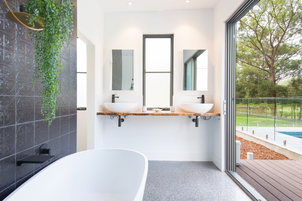 Cette photo montre une salle de bain principale tendance de taille moyenne avec une baignoire indépendante, un carrelage gris, un plan de toilette en bois, un mur blanc, un sol en terrazzo, une vasque, un sol gris et un plan de toilette marron.