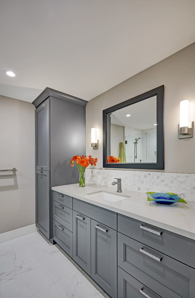 Cette image montre une salle de bain grise et blanche traditionnelle de taille moyenne avec un placard avec porte à panneau encastré, un mur gris, un lavabo encastré, des portes de placard grises, un carrelage blanc et un plan de toilette gris.