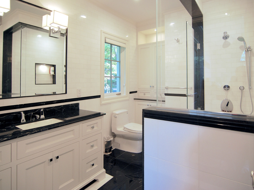 Photo of a large classic ensuite bathroom in New York with shaker cabinets, white cabinets, a corner shower, a one-piece toilet, white tiles, metro tiles, white walls, marble flooring, a submerged sink, marble worktops, black floors and a hinged door.
