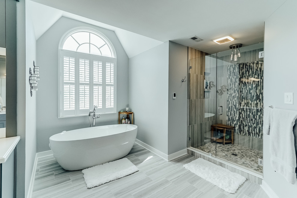 На фото: большая главная ванная комната в современном стиле с фасадами в стиле шейкер, серыми фасадами, отдельно стоящей ванной, душем в нише, унитазом-моноблоком, серой плиткой, керамогранитной плиткой, серыми стенами, полом из керамогранита, столешницей из искусственного камня, серым полом, душем с распашными дверями, белой столешницей и врезной раковиной с