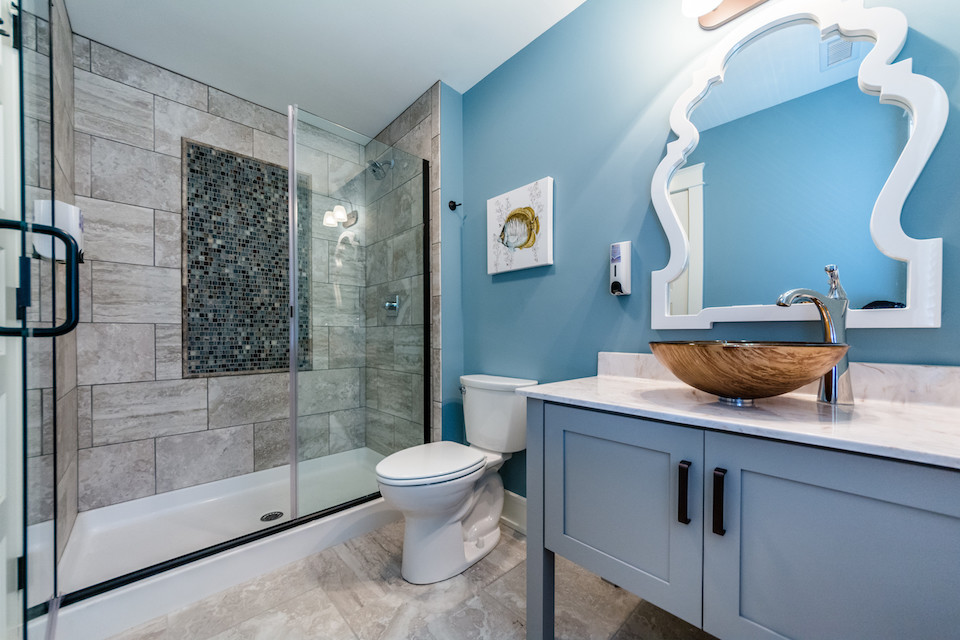 На фото: ванная комната среднего размера в морском стиле с фасадами в стиле шейкер, синими фасадами, душем в нише, раздельным унитазом, серой плиткой, керамогранитной плиткой, синими стенами, полом из керамогранита, душевой кабиной, настольной раковиной, мраморной столешницей, серым полом и душем с распашными дверями