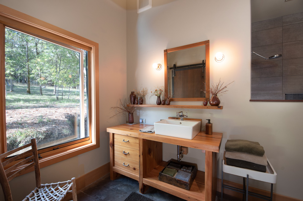 На фото: главная ванная комната в стиле рустика с фасадами цвета дерева среднего тона, бетонным полом, серым полом, серыми стенами, настольной раковиной, столешницей из дерева, коричневой столешницей и плоскими фасадами