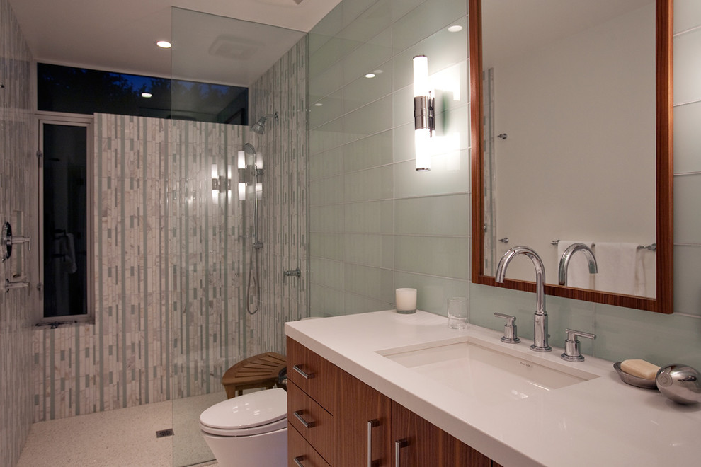 Inredning av ett 50 tals litet badrum, med släta luckor, skåp i mellenmörkt trä, en kantlös dusch, en toalettstol med hel cisternkåpa, grön kakel, mosaik, vita väggar, ett undermonterad handfat och bänkskiva i kvarts
