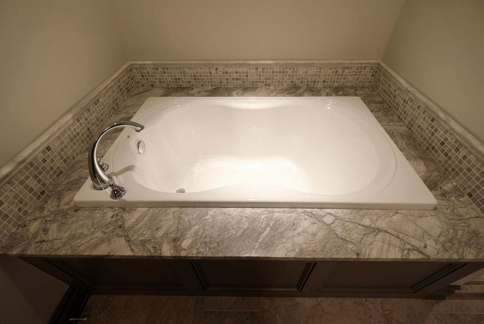 Inredning av ett klassiskt stort en-suite badrum, med luckor med infälld panel, bruna skåp, ett badkar i en alkov, grå kakel, grå väggar och granitbänkskiva