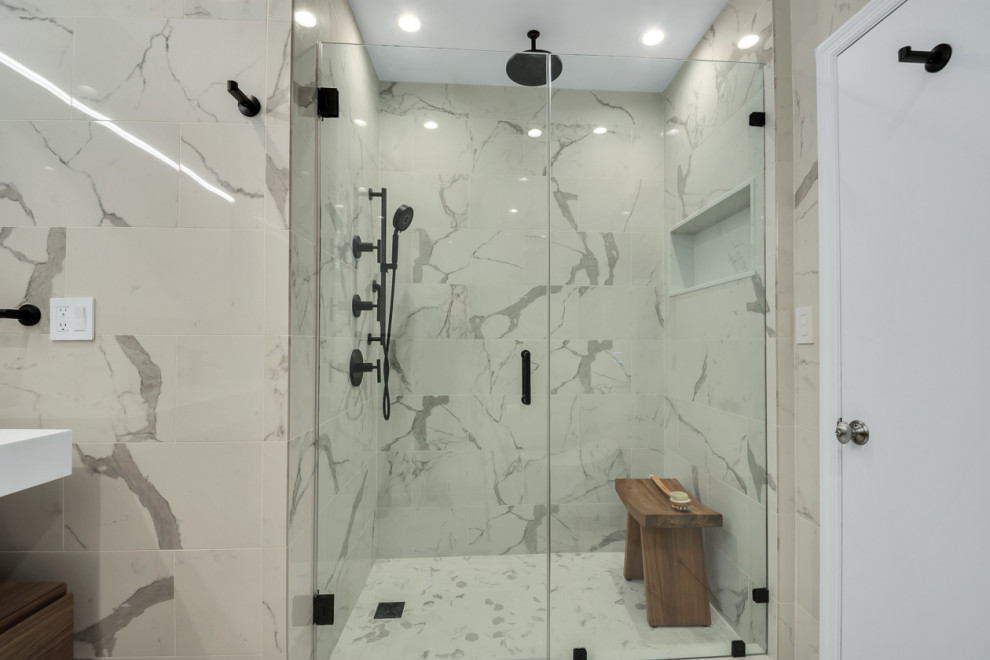 This is an example of a large modern ensuite bathroom in New York with flat-panel cabinets, brown cabinets, a built-in bath, a shower/bath combination, a bidet, multi-coloured tiles, porcelain tiles, white walls, porcelain flooring, a pedestal sink, limestone worktops, white floors, a hinged door, white worktops, a wall niche, double sinks and a floating vanity unit.