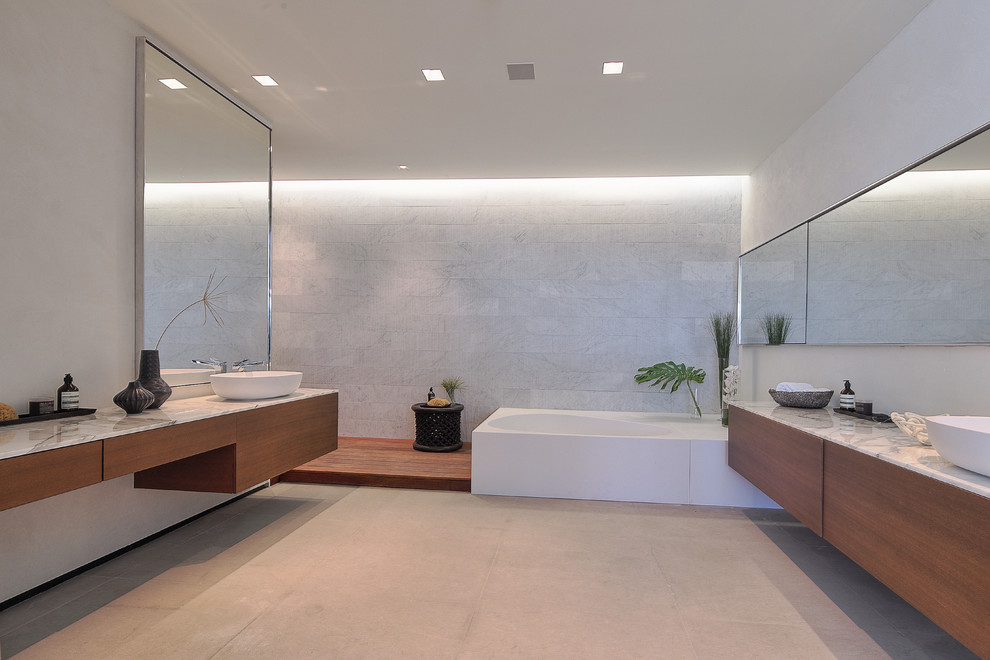Diseño de cuarto de baño actual con puertas de armario de madera clara, paredes beige, encimera de mármol y microcemento