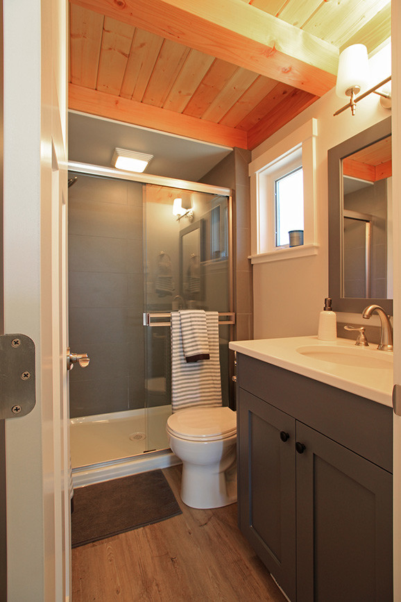 Aménagement d'une petite salle de bain craftsman avec un placard à porte shaker, des portes de placard bleues, WC à poser, un carrelage gris, des carreaux de porcelaine, un mur gris, un sol en vinyl, un lavabo encastré et un plan de toilette en quartz modifié.