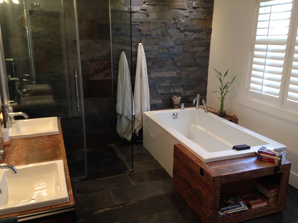 Inspiration pour une salle de bain principale chalet en bois brun de taille moyenne avec une baignoire encastrée, une douche d'angle, un carrelage noir, un carrelage de pierre, un mur noir, un sol en calcaire, un lavabo posé et un plan de toilette en bois.