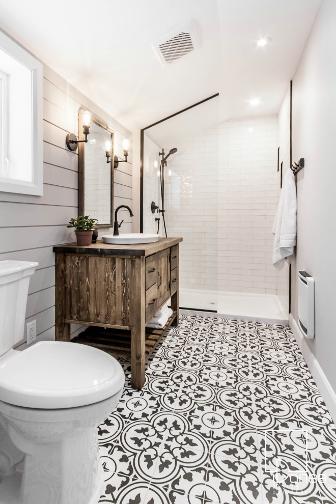 This is an example of a medium sized vintage ensuite bathroom in Montreal with flat-panel cabinets, a freestanding vanity unit, medium wood cabinets, a walk-in shower, a two-piece toilet, white tiles, cement tiles, beige walls, porcelain flooring, a vessel sink, wooden worktops, black floors, an open shower, brown worktops, a wall niche, a single sink and tongue and groove walls.