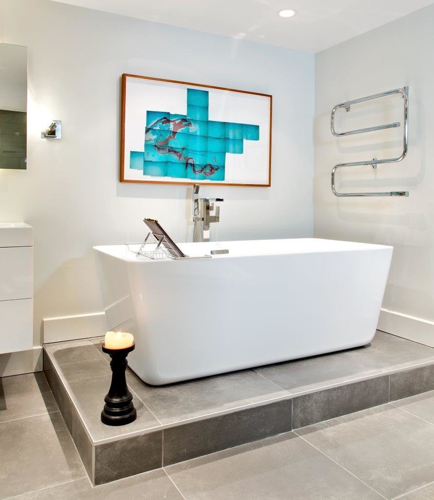 This is an example of a contemporary bathroom in Montreal with a freestanding bath and grey tiles.