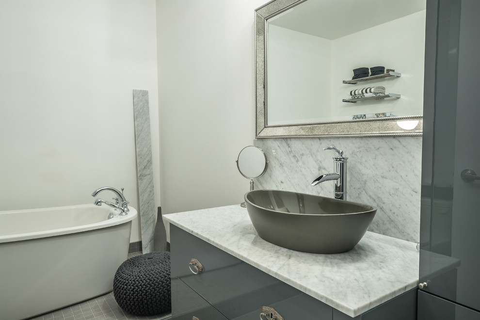 This is an example of a medium sized contemporary ensuite bathroom in Montreal with flat-panel cabinets, grey cabinets, a freestanding bath, grey tiles, marble tiles, white walls, ceramic flooring, a vessel sink, marble worktops, grey floors and grey worktops.
