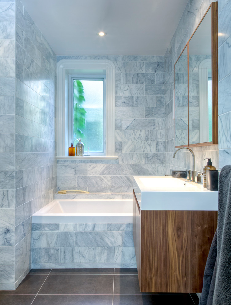 Modernes Badezimmer mit integriertem Waschbecken, flächenbündigen Schrankfronten, hellbraunen Holzschränken, Badewanne in Nische und grauen Fliesen in Montreal