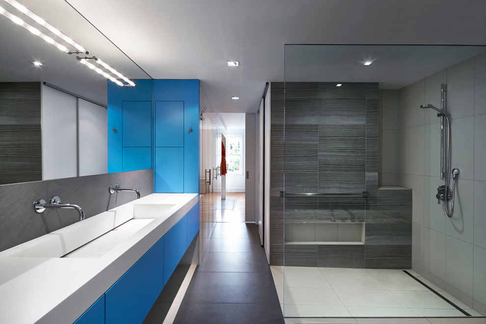 Bild på ett funkis badrum med dusch, med ett avlångt handfat, släta luckor, blå skåp, en kantlös dusch och grå kakel