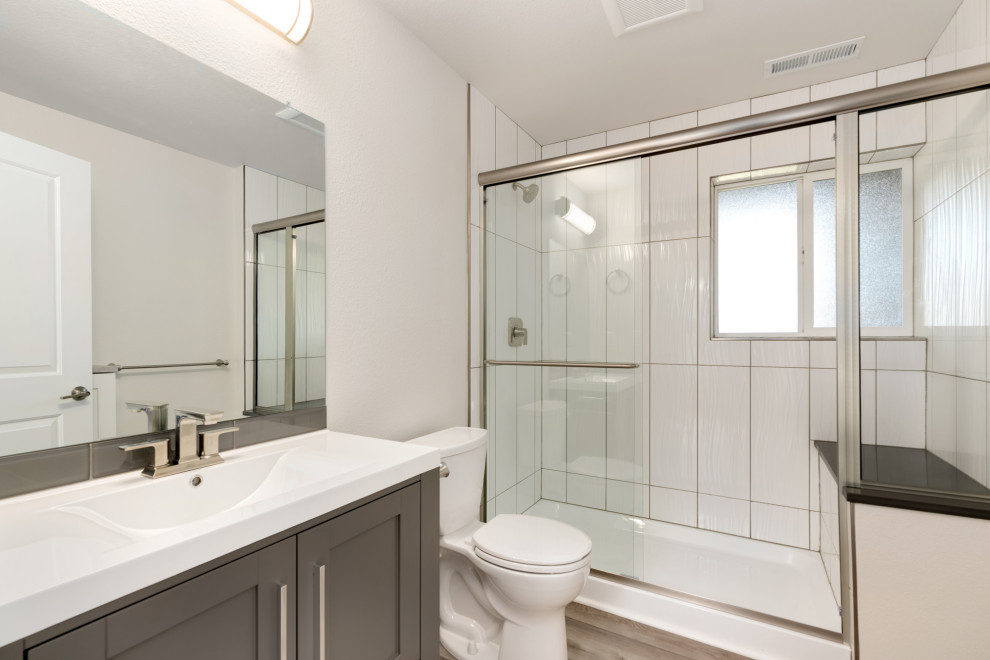 Exempel på ett mellanstort modernt vit vitt badrum med dusch, med skåp i shakerstil, grå skåp, en dusch i en alkov, en toalettstol med separat cisternkåpa, vit kakel, keramikplattor, vinylgolv, ett integrerad handfat, bänkskiva i kvarts, grått golv och dusch med skjutdörr