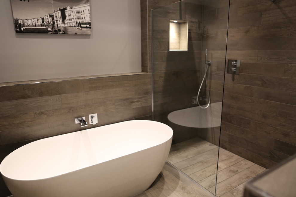 Large modern wet room bathroom in Essex with freestanding cabinets, medium wood cabinets, a freestanding bath, a wall mounted toilet, grey tiles, porcelain tiles, grey walls, porcelain flooring, a vessel sink, wooden worktops, grey floors and an open shower.