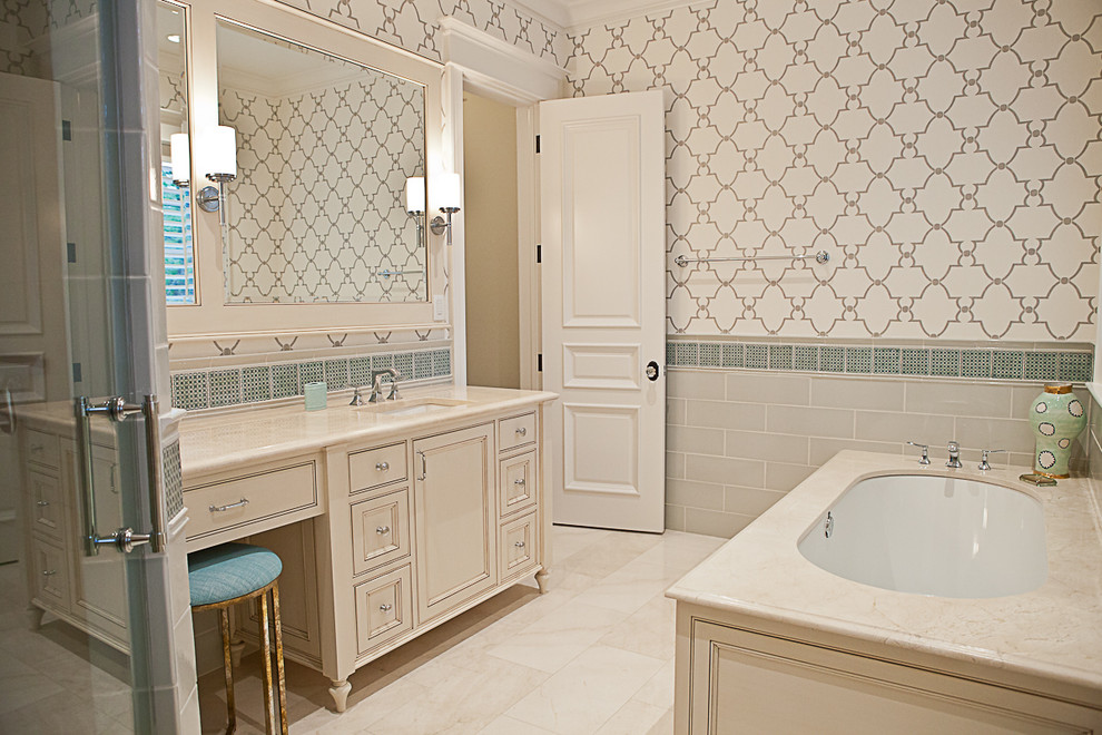 Cette image montre une salle de bain principale traditionnelle avec un placard avec porte à panneau surélevé, des portes de placard beiges, une baignoire en alcôve, un carrelage beige, un sol en marbre, un lavabo encastré et un plan de toilette en granite.