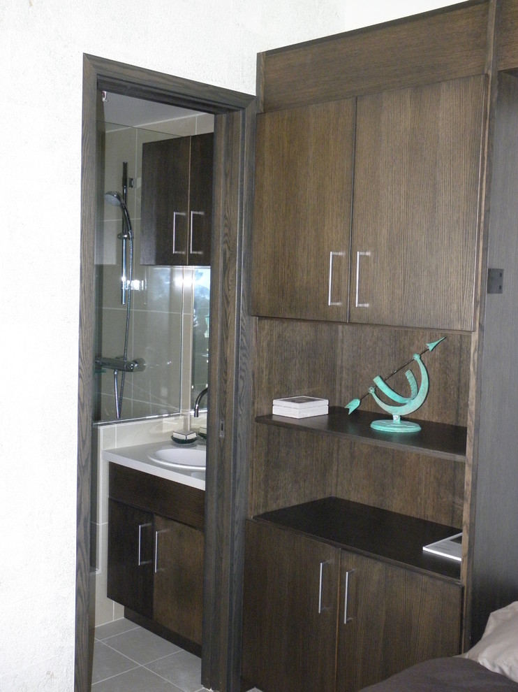 Example of a small zen 3/4 beige tile and ceramic tile ceramic tile and gray floor alcove shower design in Hawaii with flat-panel cabinets, black cabinets, a one-piece toilet, beige walls, a drop-in sink, solid surface countertops and a hinged shower door