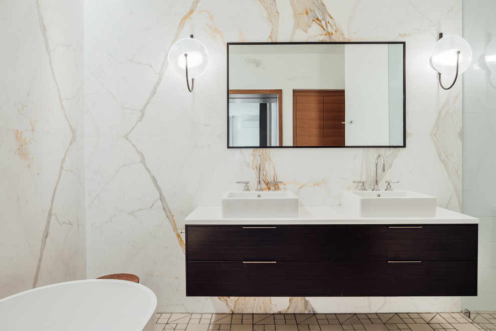 На фото: большая главная ванная комната в стиле модернизм с плоскими фасадами, темными деревянными фасадами, отдельно стоящей ванной, мраморной плиткой, полом из керамической плитки, столешницей из искусственного камня и белой столешницей