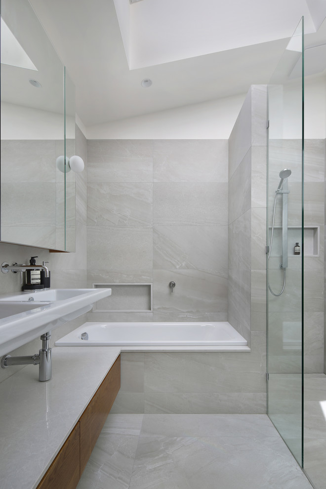Modern inredning av ett mellanstort badrum med dusch, med beige skåp, ett platsbyggt badkar, en öppen dusch, keramikplattor, klinkergolv i keramik, bänkskiva i kvarts, med dusch som är öppen, grå kakel, grå väggar, ett väggmonterat handfat, grått golv och släta luckor