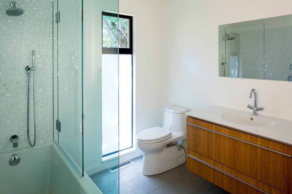 サンフランシスコにある中くらいなコンテンポラリースタイルのおしゃれな浴室 (一体型シンク、磁器タイル、フラットパネル扉のキャビネット、中間色木目調キャビネット、シャワー付き浴槽	、一体型トイレ	、白いタイル、白い壁、磁器タイルの床) の写真