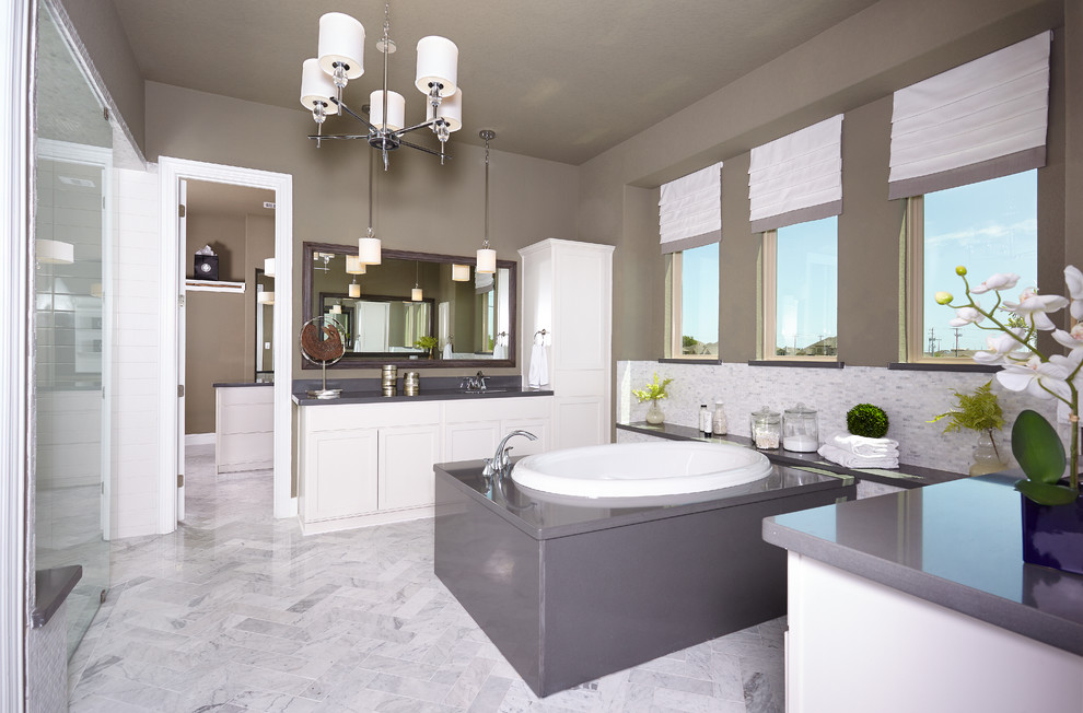 Inredning av ett mycket stort en-suite badrum, med luckor med infälld panel, vita skåp, ett platsbyggt badkar, en dubbeldusch, grå kakel, stenkakel, grå väggar, klinkergolv i keramik, ett undermonterad handfat, bänkskiva i akrylsten, grått golv och dusch med skjutdörr