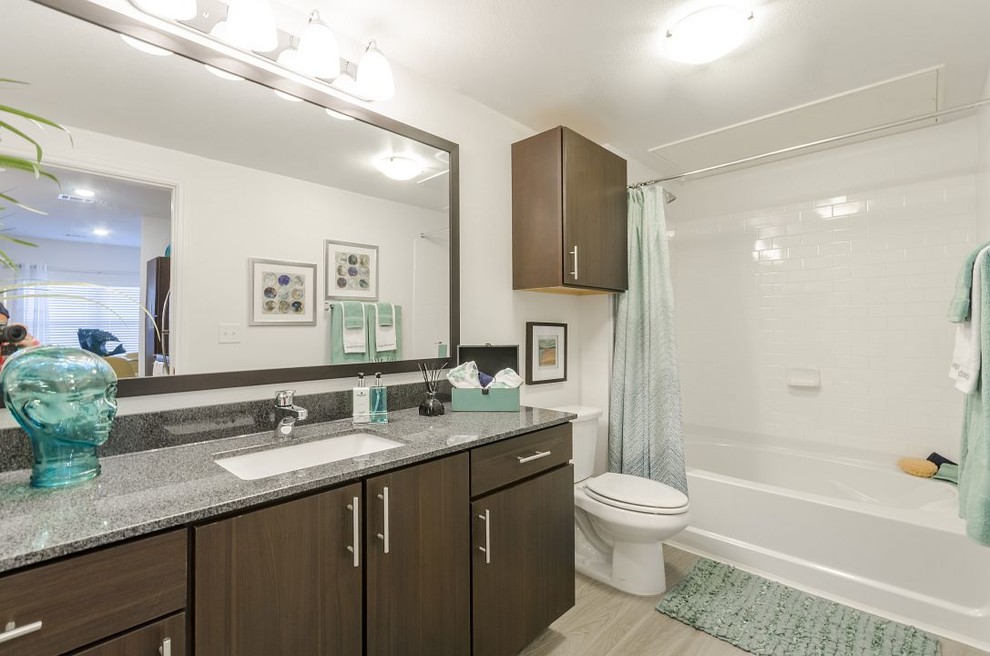 Inspiration for a mid-sized contemporary 3/4 white tile and subway tile medium tone wood floor and brown floor bathroom remodel in Austin with flat-panel cabinets, dark wood cabinets, a two-piece toilet, beige walls, an undermount sink and granite countertops