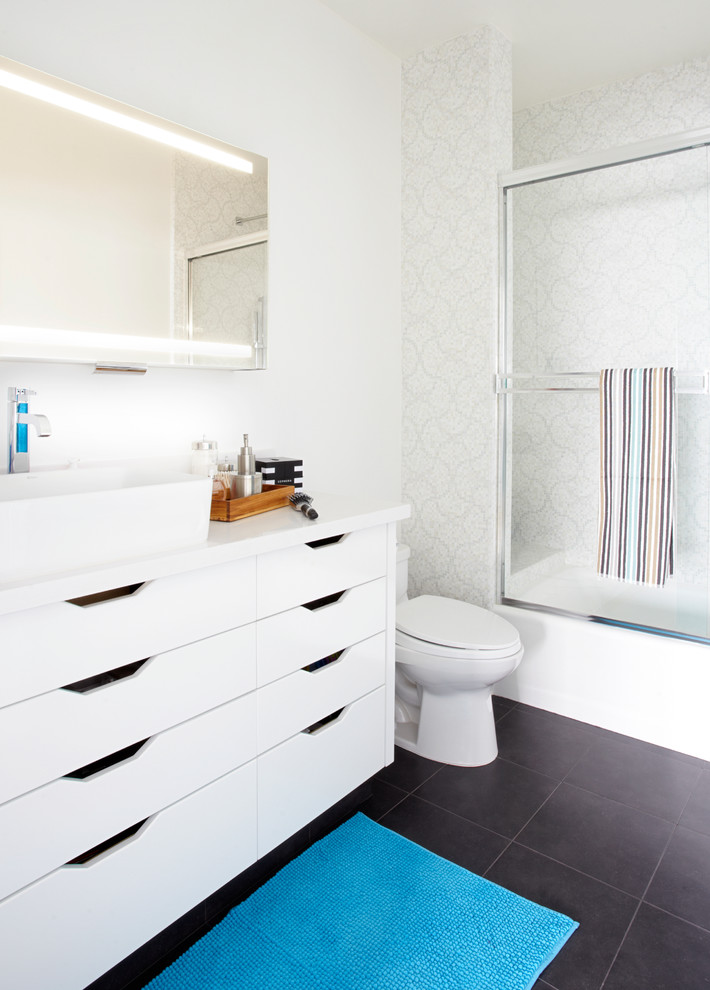 Photo of a medium sized contemporary bathroom in Orange County with a vessel sink, flat-panel cabinets, white cabinets, an alcove bath, a shower/bath combination, a two-piece toilet, white walls, porcelain flooring, solid surface worktops, black floors, a sliding door and white worktops.