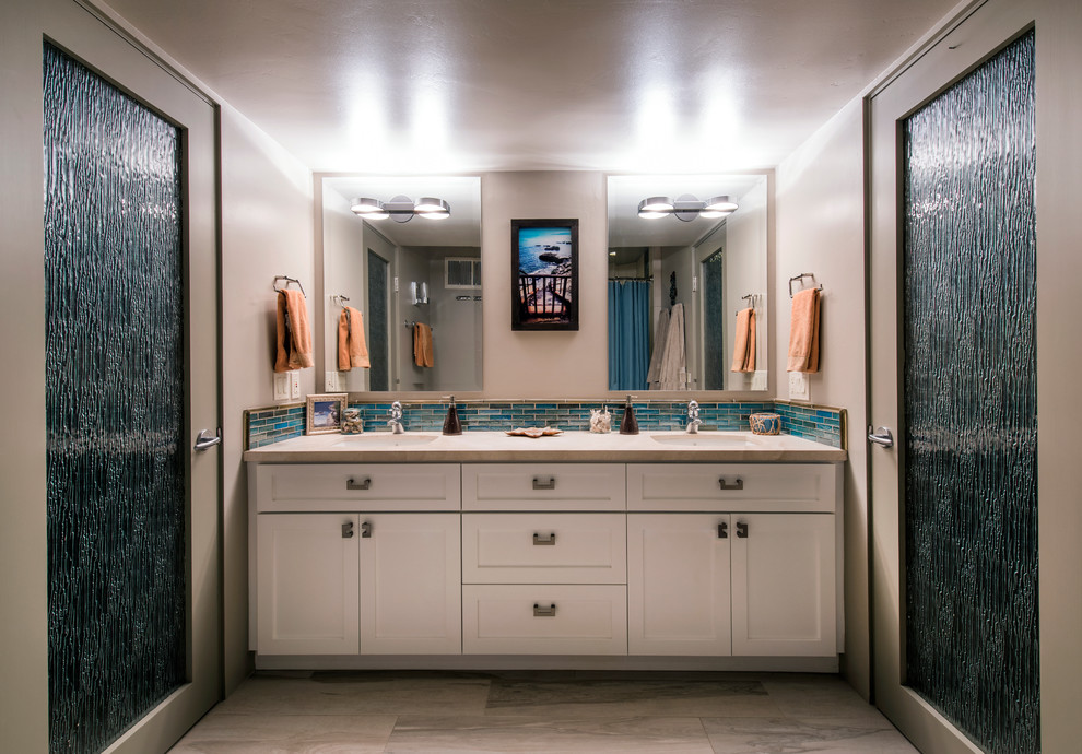 サンディエゴにある高級な中くらいなビーチスタイルのおしゃれなマスターバスルーム (アンダーカウンター洗面器、落し込みパネル扉のキャビネット、白いキャビネット、ライムストーンの洗面台、青いタイル、ガラスタイル、ベージュの壁、ライムストーンの床) の写真