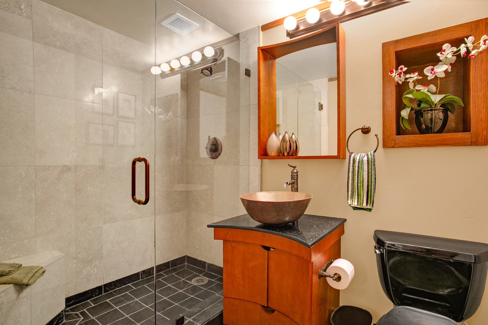 Example of a mid-sized zen 3/4 black tile and travertine tile slate floor bathroom design in San Diego with flat-panel cabinets, medium tone wood cabinets, a two-piece toilet, beige walls, a vessel sink and granite countertops