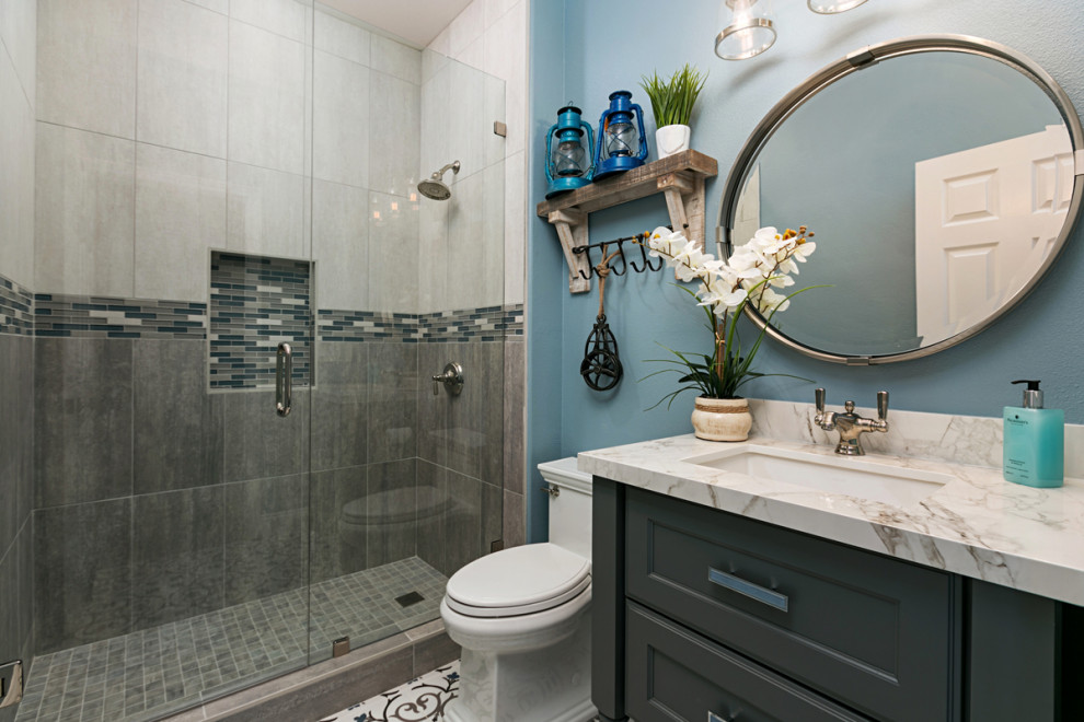 Inspiration for a small transitional 3/4 gray tile and stone tile porcelain tile and white floor alcove shower remodel in San Diego with furniture-like cabinets, gray cabinets, a one-piece toilet, blue walls, an undermount sink, quartz countertops, a hinged shower door and white countertops