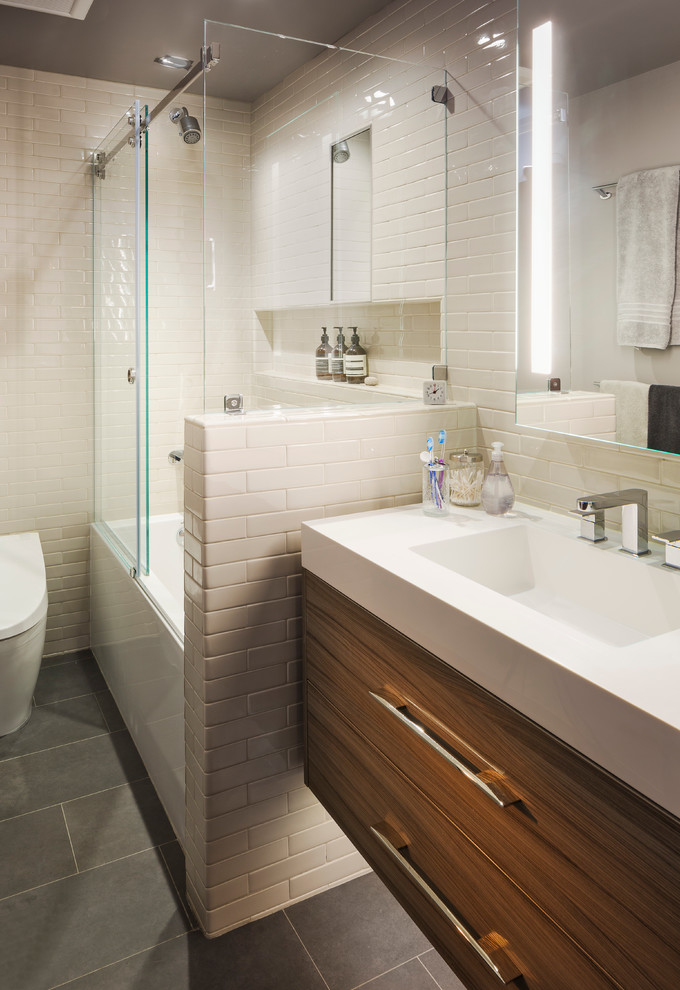 Idéer för ett litet modernt vit badrum, med släta luckor, skåp i mellenmörkt trä, ett badkar i en alkov, en dusch/badkar-kombination, en vägghängd toalettstol, vit kakel, tunnelbanekakel, vita väggar, skiffergolv, ett integrerad handfat, bänkskiva i akrylsten, grått golv och dusch med skjutdörr