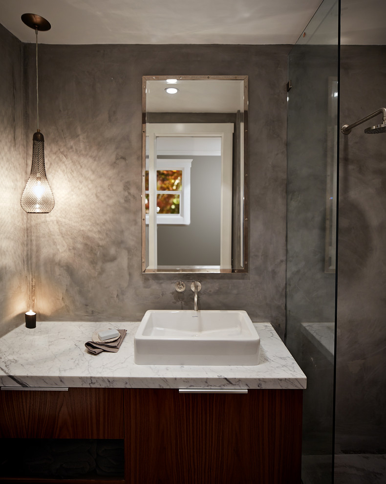 Cette image montre une petite salle de bain principale design en bois brun avec un placard à porte plane, un plan de toilette en marbre et un mur gris.
