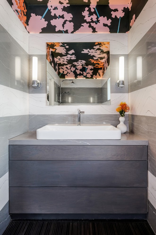 Cette image montre une salle de bain design avec un placard à porte plane, des portes de placard grises, un carrelage gris, un carrelage blanc, du carrelage en marbre, un mur multicolore, une vasque, un sol marron et un plan de toilette gris.
