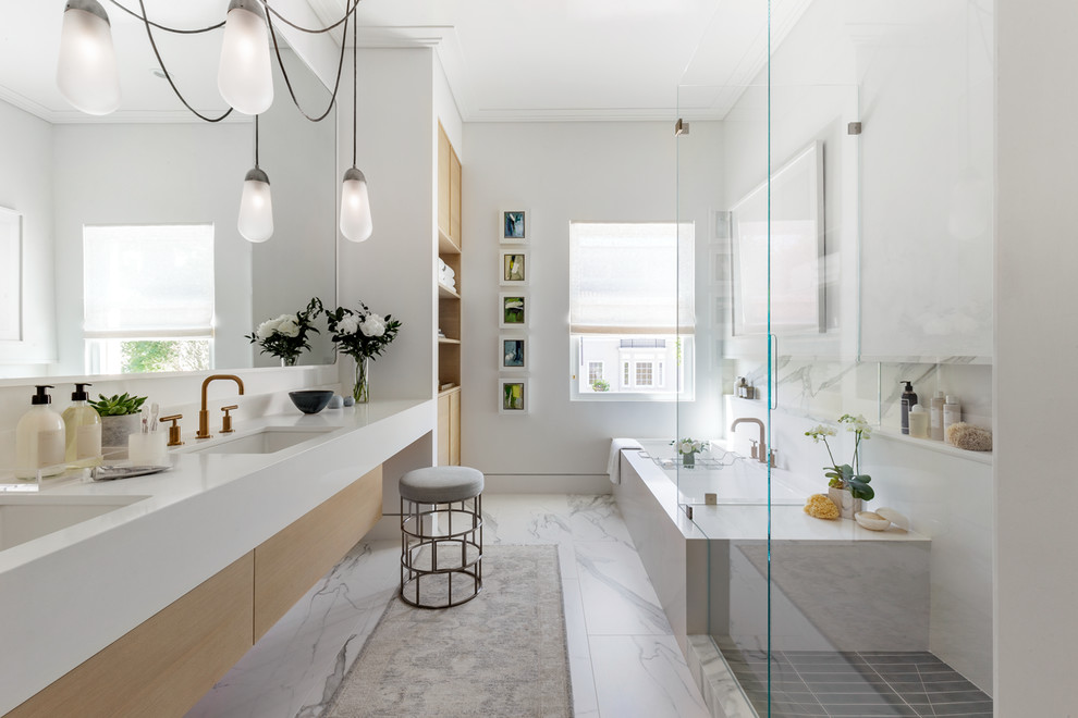 Modern inredning av ett en-suite badrum, med släta luckor, skåp i ljust trä, ett undermonterat badkar, vit kakel, vita väggar, marmorgolv, ett undermonterad handfat, vitt golv och dusch med gångjärnsdörr