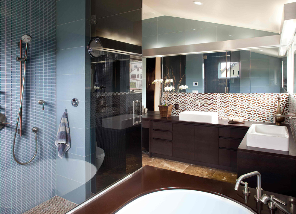Пример оригинального дизайна: огромная главная ванная комната в современном стиле с настольной раковиной, плоскими фасадами, темными деревянными фасадами, полновстраиваемой ванной, душем без бортиков, синей плиткой, стеклянной плиткой, столешницей из дерева, синими стенами, мраморным полом и коричневой столешницей
