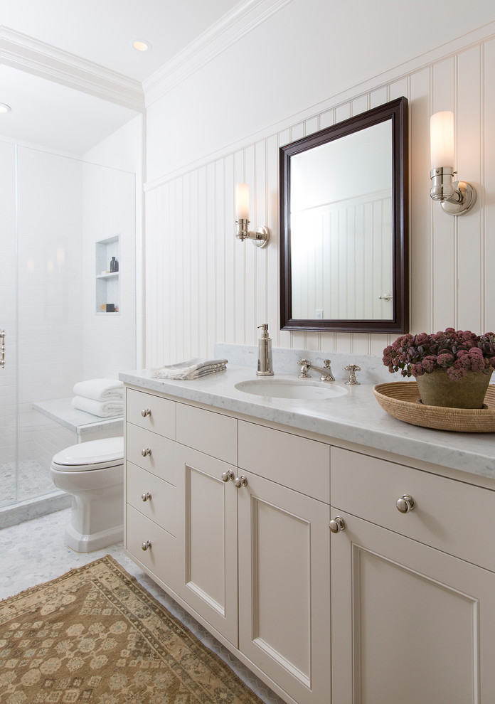 Exemple d'une douche en alcôve chic avec un placard à porte affleurante, des portes de placard blanches, WC à poser, un carrelage blanc, un mur blanc, un sol en marbre, un lavabo encastré, un plan de toilette en marbre, un sol blanc, une cabine de douche à porte battante et un plan de toilette blanc.