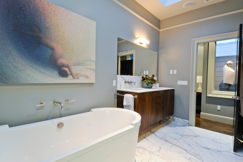 Modelo de cuarto de baño actual con lavabo bajoencimera, armarios con paneles lisos, puertas de armario de madera en tonos medios, bañera exenta y encimeras blancas