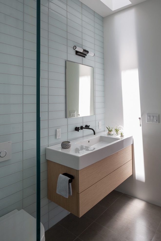 Inspiration för ett mellanstort funkis vit vitt badrum med dusch, med släta luckor, skåp i ljust trä, glaskakel, en vägghängd toalettstol, vita väggar, ett integrerad handfat, grått golv och klinkergolv i porslin