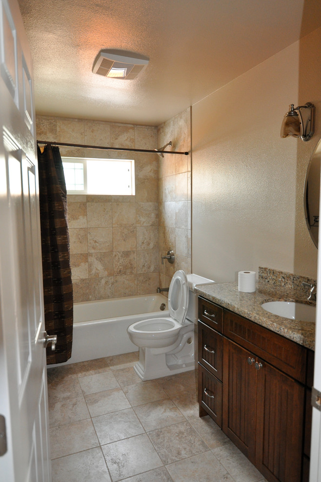 Inredning av ett klassiskt badrum, med ett undermonterad handfat, luckor med infälld panel, skåp i mörkt trä, granitbänkskiva, ett badkar i en alkov, en dusch/badkar-kombination, en toalettstol med separat cisternkåpa, beige kakel och keramikplattor