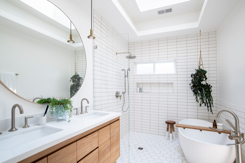 Exemple d'une salle de bain nature en bois brun avec un placard à porte plane, une baignoire indépendante, un espace douche bain, un carrelage blanc, un mur blanc, un lavabo encastré, un sol blanc, aucune cabine, un plan de toilette blanc, une niche, meuble double vasque et un plafond décaissé.