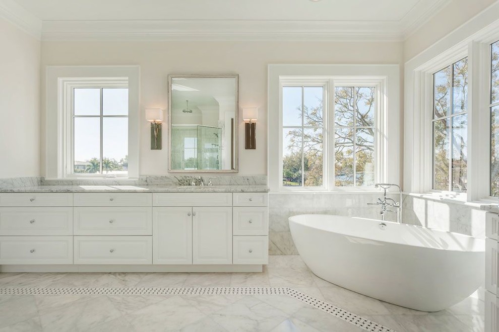 Idée de décoration pour une grande salle de bain principale minimaliste avec un lavabo encastré, un placard avec porte à panneau surélevé, des portes de placard blanches, un plan de toilette en marbre, une baignoire indépendante, un carrelage blanc, un carrelage de pierre, un mur blanc, un sol en marbre et un sol blanc.