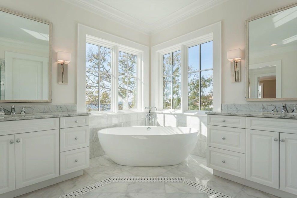 This is an example of a large mediterranean ensuite bathroom in Tampa with a submerged sink, raised-panel cabinets, white cabinets, marble worktops, a freestanding bath, white tiles, stone tiles, white walls, marble flooring and white floors.