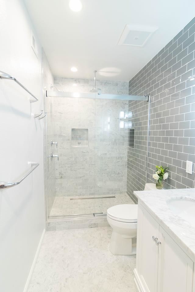 Пример оригинального дизайна: ванная комната среднего размера в стиле неоклассика (современная классика) с фасадами с утопленной филенкой, белыми фасадами, душем в нише, унитазом-моноблоком, серой плиткой, керамогранитной плиткой, белыми стенами, полом из керамогранита, душевой кабиной, врезной раковиной, столешницей из искусственного кварца, белым полом, душем с раздвижными дверями и белой столешницей