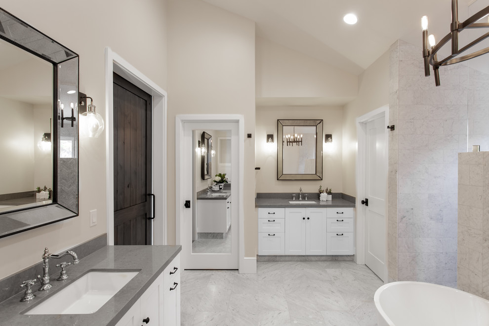 Idée de décoration pour une salle de bain principale tradition avec un placard à porte shaker, des portes de placard blanches, une baignoire indépendante, un carrelage beige, un lavabo encastré, un sol gris et un plan de toilette gris.