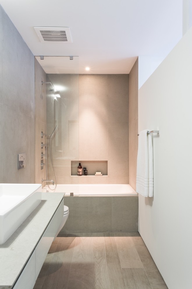 Bild på ett litet funkis badrum med dusch, med ett avlångt handfat, möbel-liknande, ett platsbyggt badkar, en dusch/badkar-kombination, en vägghängd toalettstol, beige kakel, keramikplattor, vita väggar, ljust trägolv, vita skåp, bänkskiva i kvarts och med dusch som är öppen