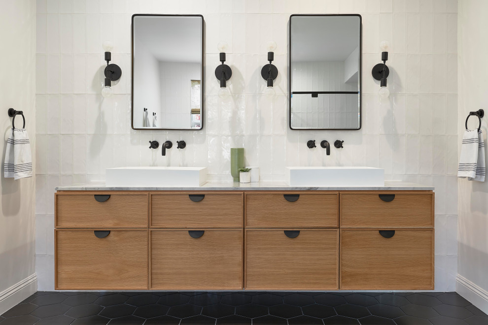 Идея дизайна: главная ванная комната в современном стиле с плоскими фасадами, фасадами цвета дерева среднего тона, белой плиткой, настольной раковиной, мраморной столешницей, черным полом и белой столешницей