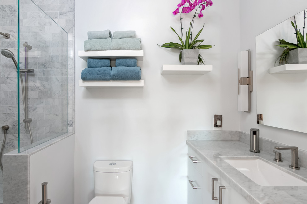 Bild på ett mellanstort funkis grå grått badrum med dusch, med släta luckor, vita skåp, en dusch i en alkov, en toalettstol med hel cisternkåpa, vita väggar, ett undermonterad handfat, marmorbänkskiva och med dusch som är öppen